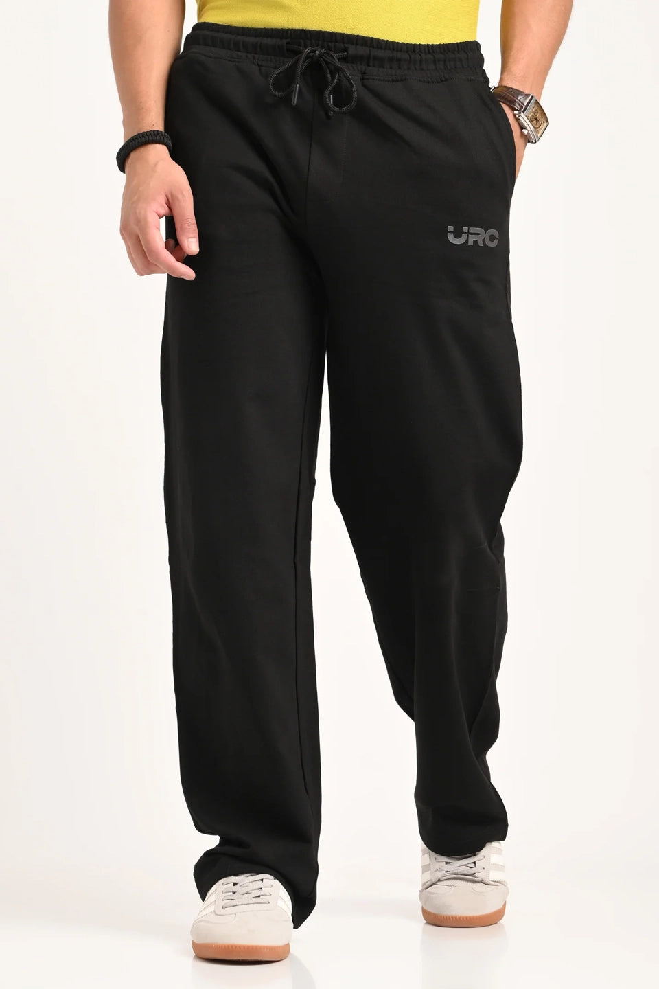 A man wearing black relaxed-fit drawstring trousers with a small "URC" logo and white sneakers.