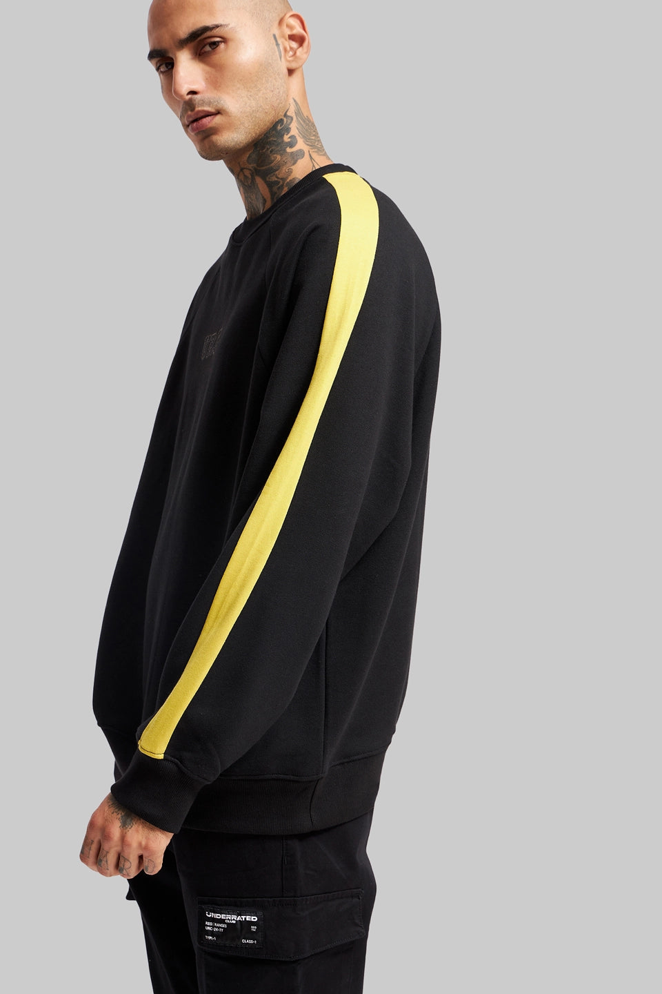Side view of a man wearing a black oversized sweatshirt with a single bold yellow stripe running down the sleeve.