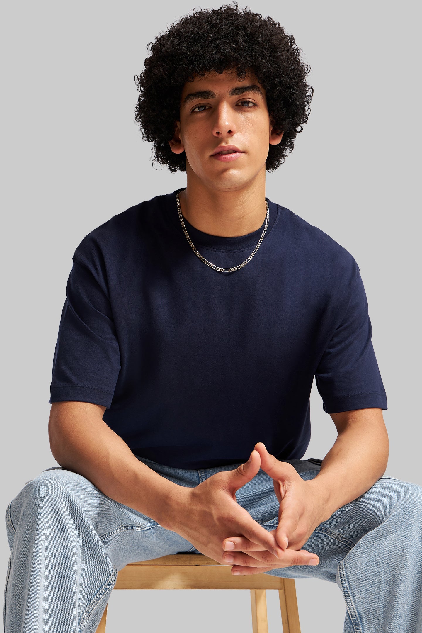 Navy blue short sleeve t-shirt afro model seated on chair blue jeans Underrated Club streetwear.