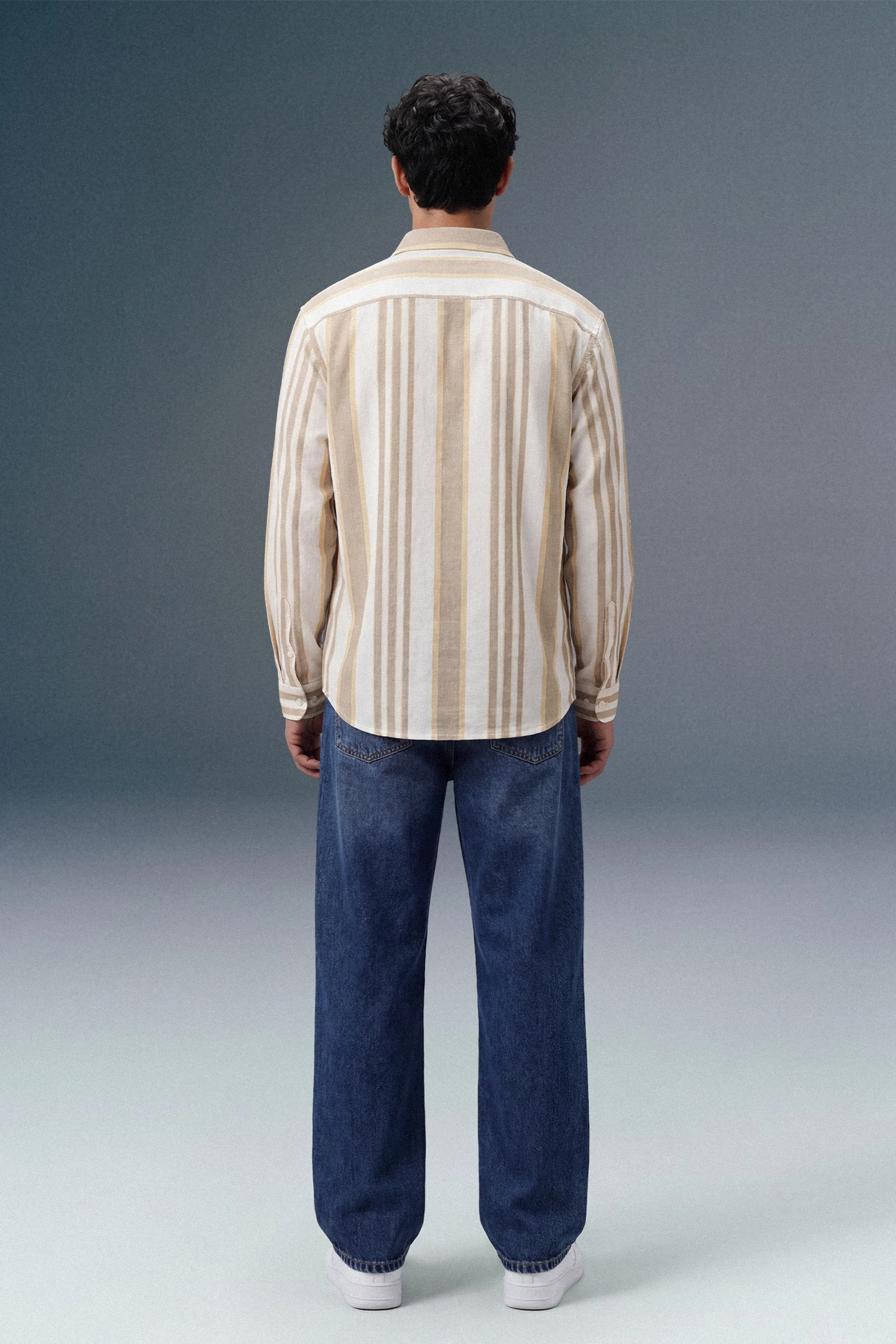 Person wearing a striped shirt and blue jeans from behind on a gray background