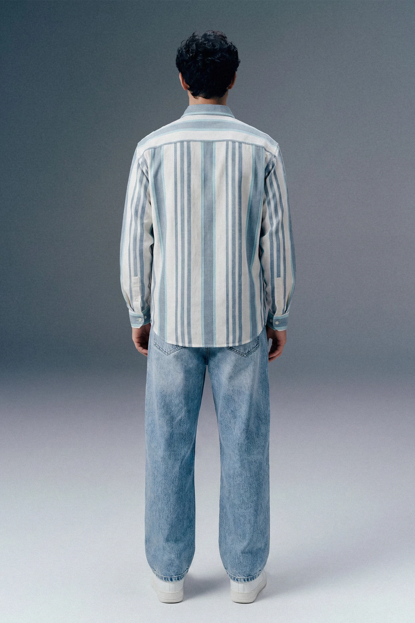 Person wearing a striped shirt and jeans from behind on a gray background