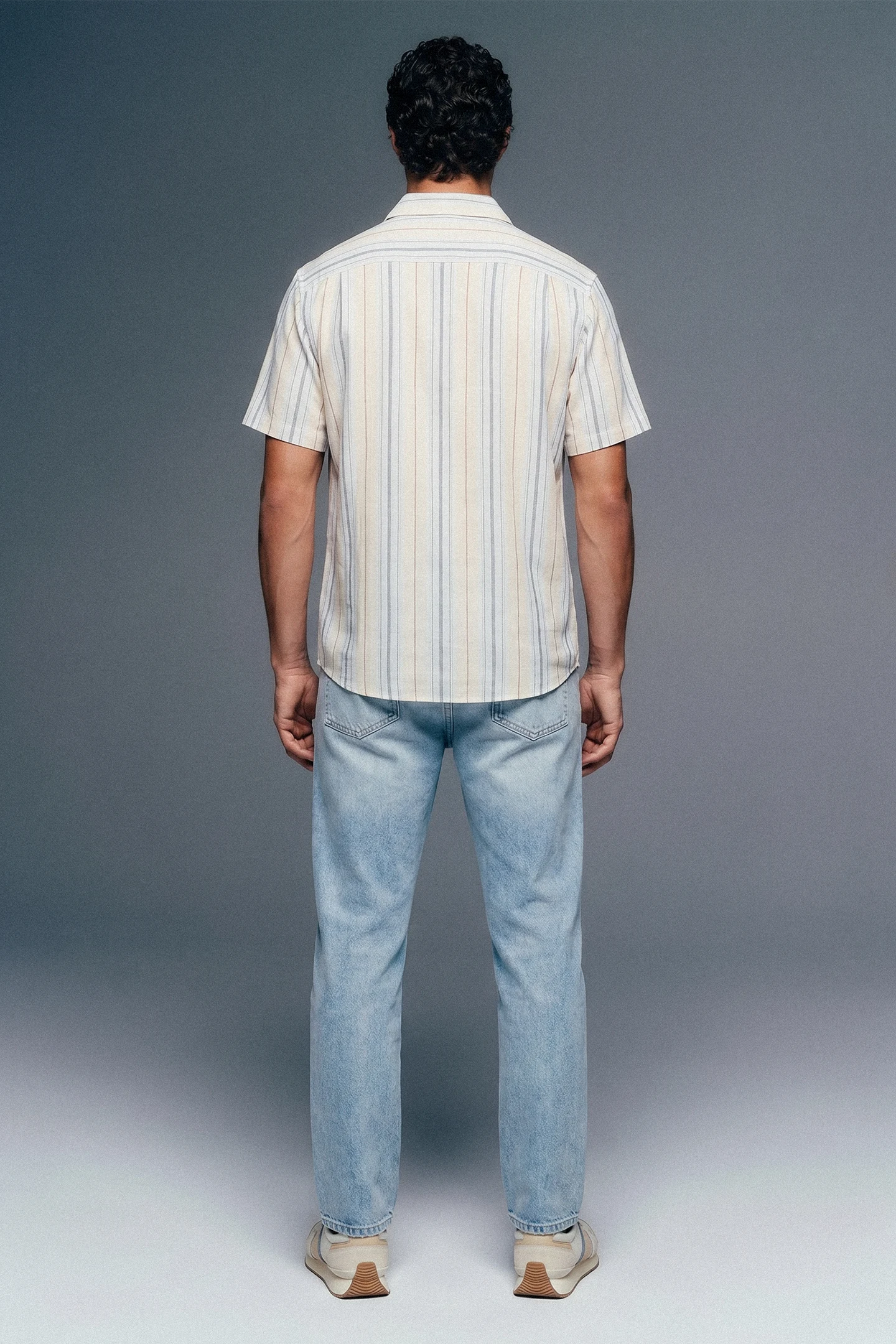 Person wearing a striped shirt and jeans from behind on a gray background