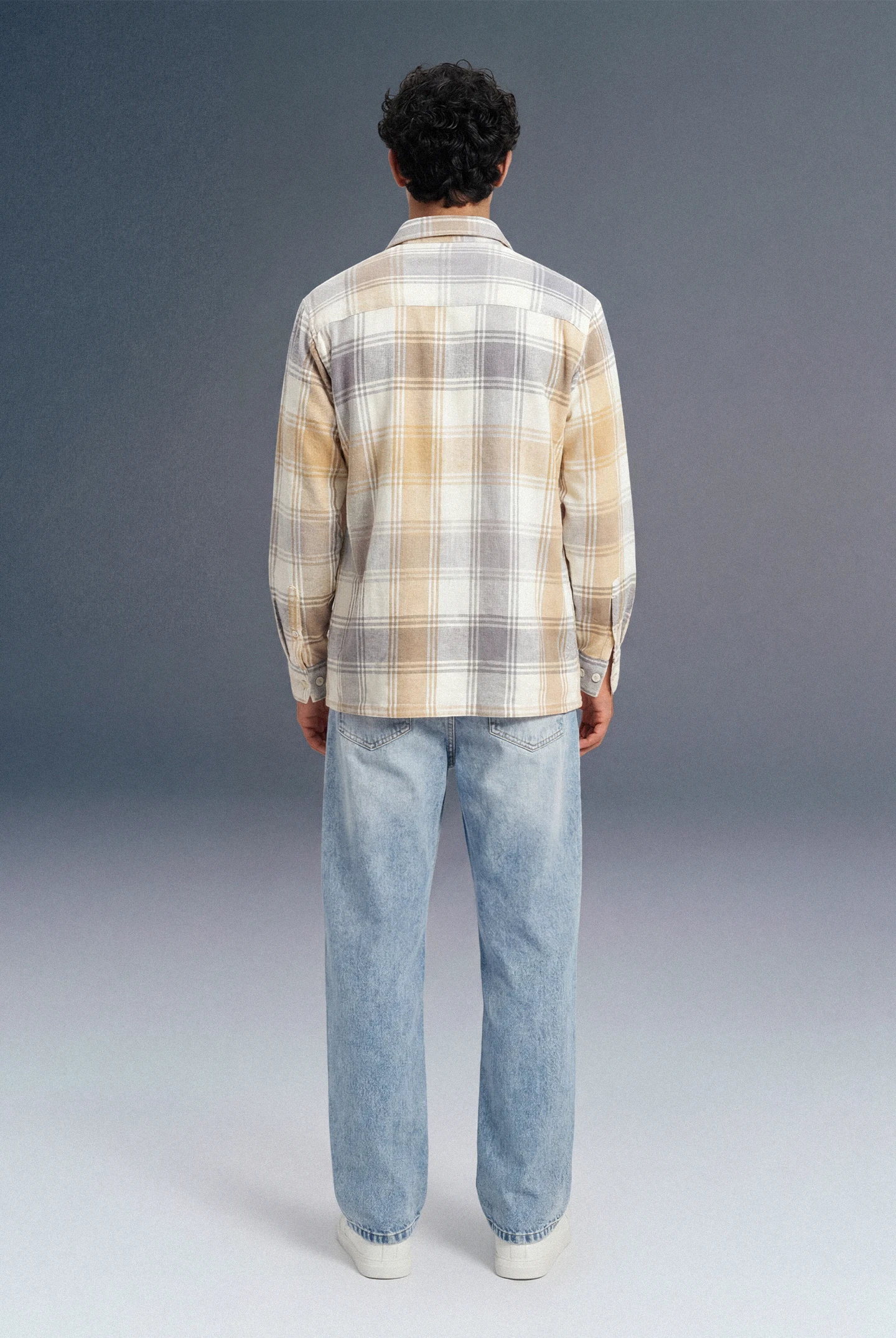 Person wearing a plaid shirt and jeans from behind on a gray background