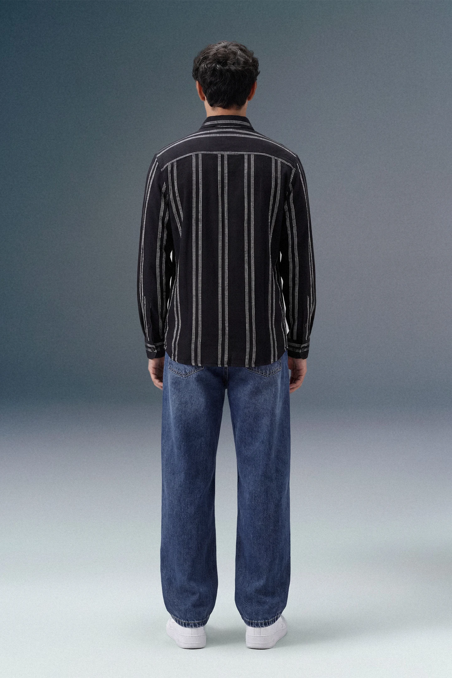 Person wearing a black and white striped shirt and blue jeans on a gray background