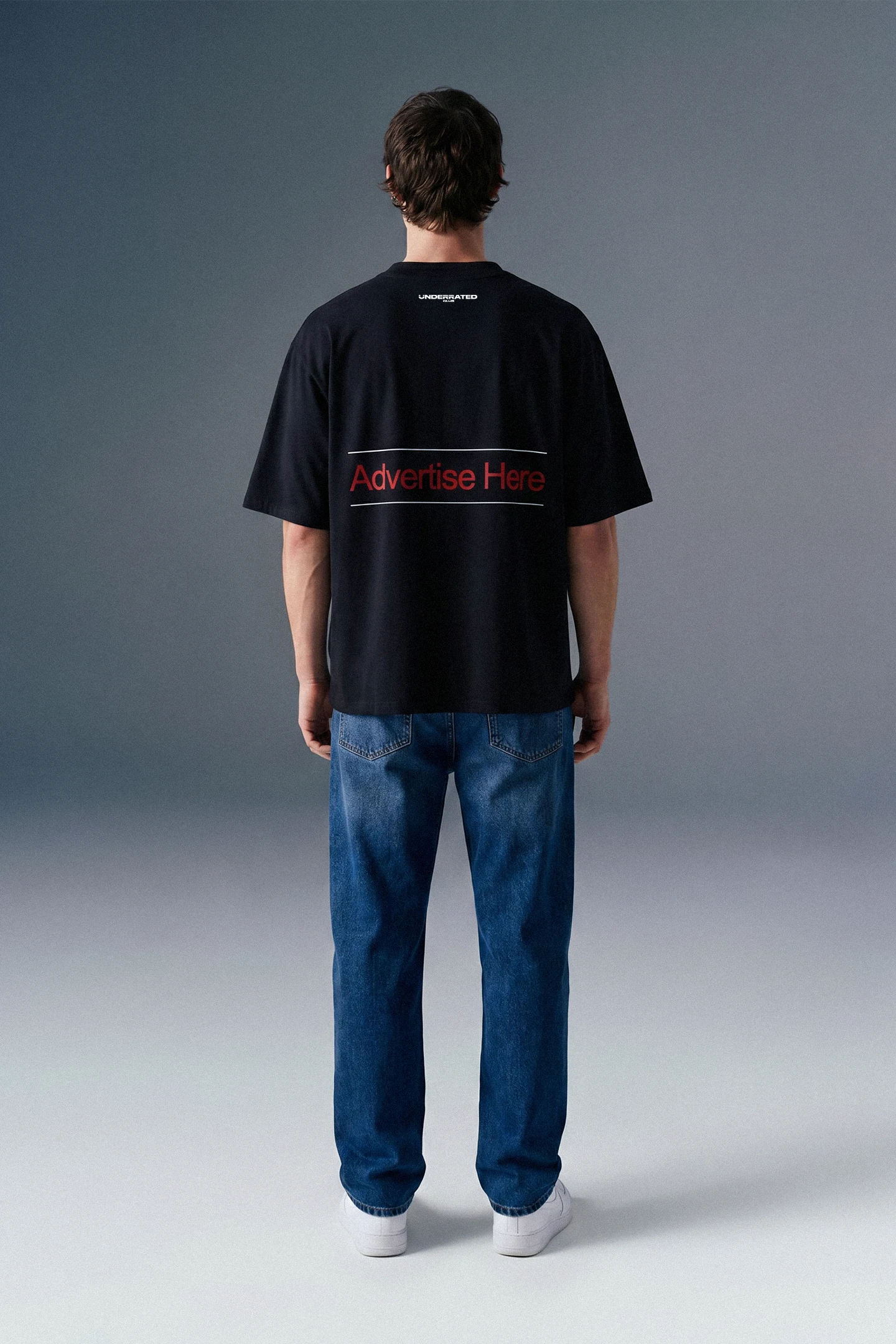 Full-length rear view of a man standing still, showcasing the complete back profile of a black graphic T-shirt paired with blue jeans.