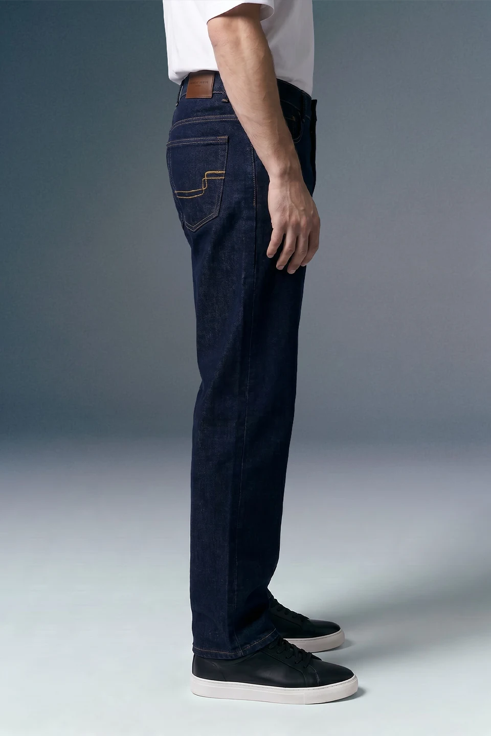 Person wearing dark blue jeans and black shoes on a gray background
