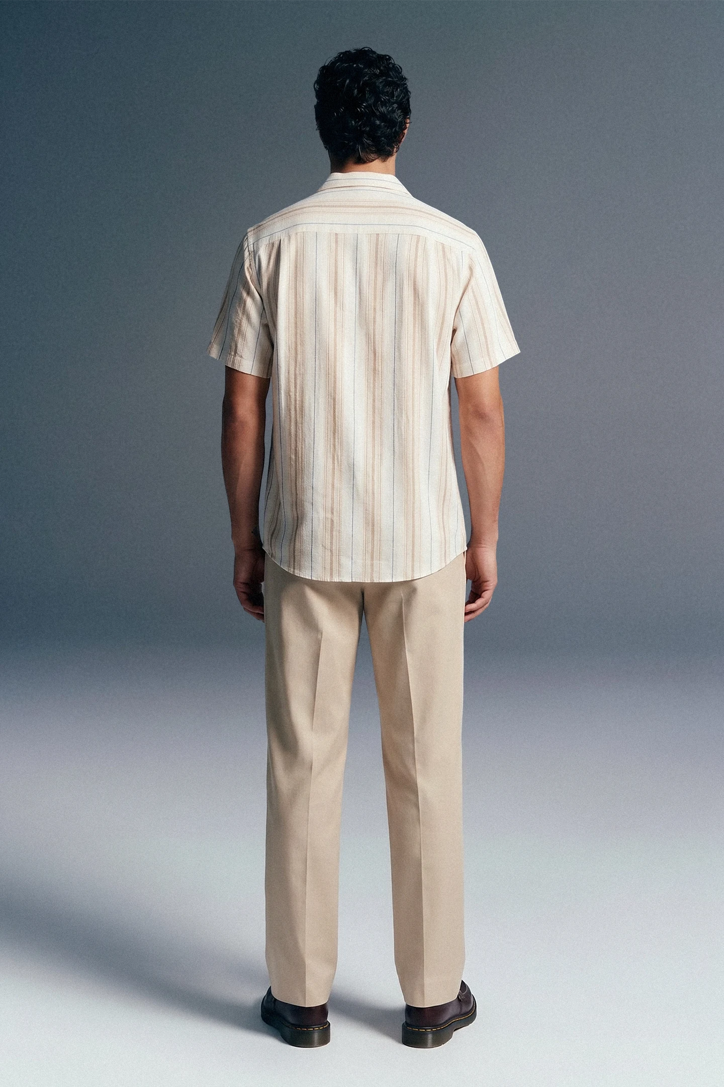 Man wearing a striped shirt and beige pants against a gray background