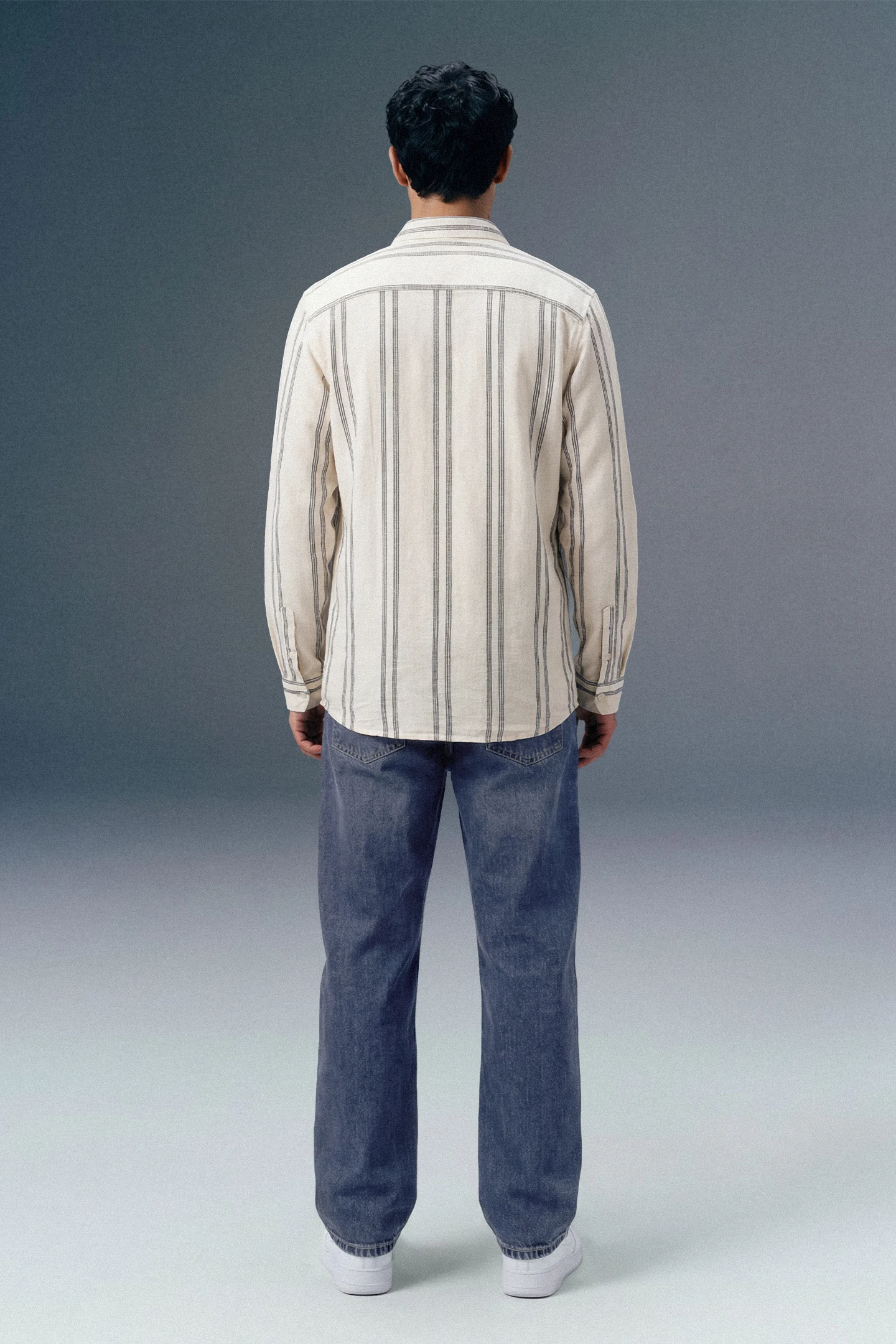 Person wearing a striped shirt and jeans from behind on a gray background