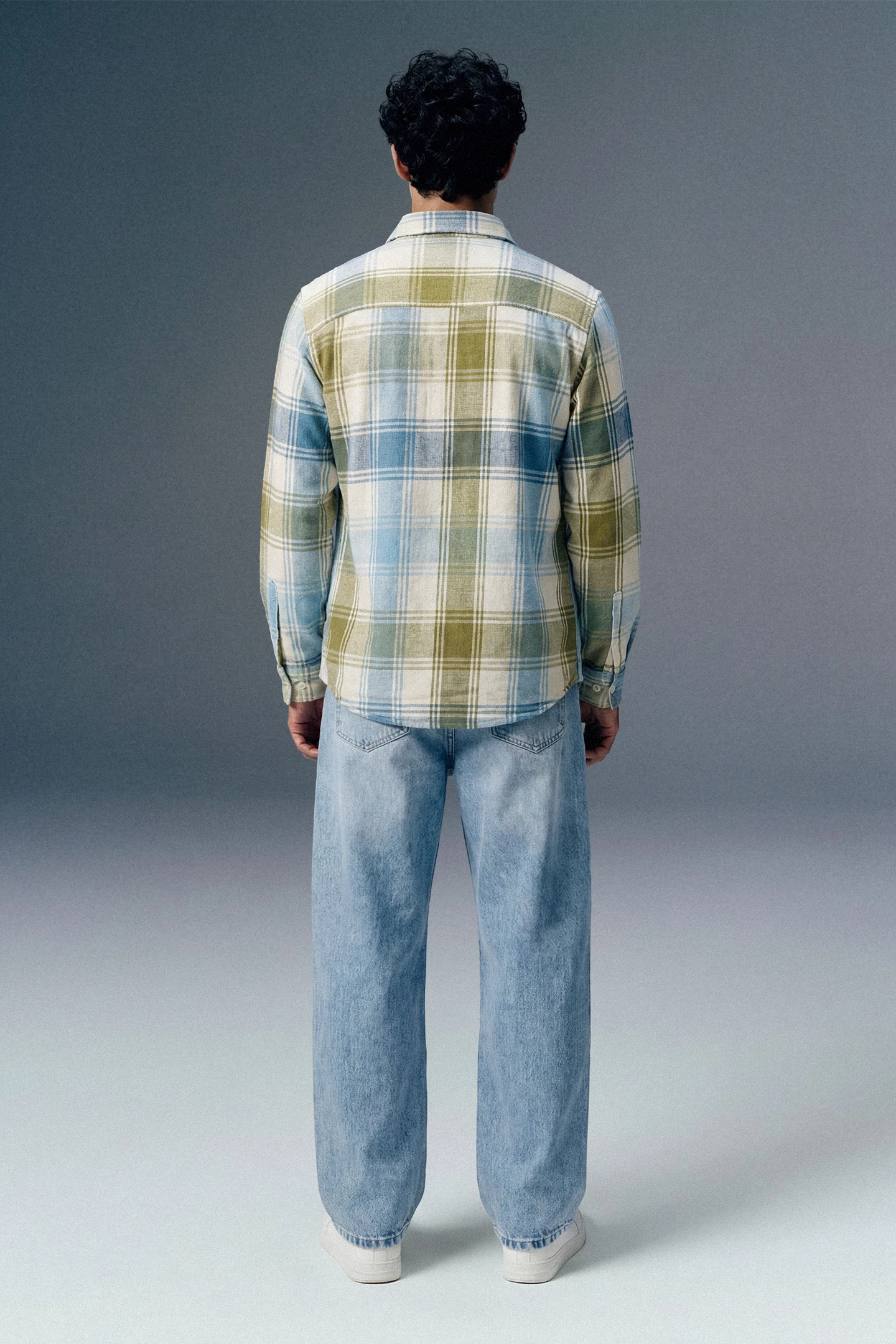 Person wearing a plaid shirt and jeans from behind on a gray background