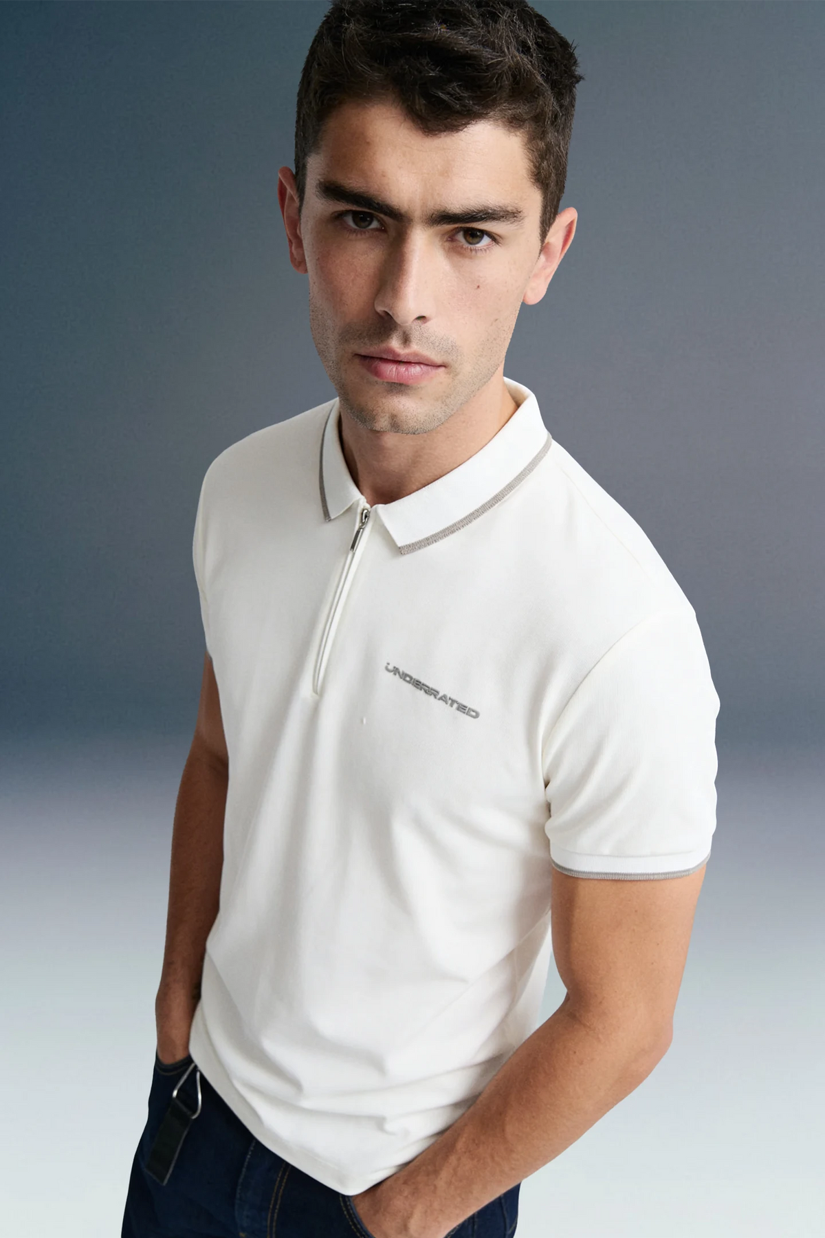 A close-up, high-angle front view of a man wearing an off-white polo shirt, showcasing a thin contrast stripe along the collar edge and subtle branding on the left chest.
