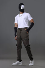 Front view of man wearing black smiley mask, white t-shirt with chain necklace, charcoal grey UNDERRATED cargo pants, wristbands, and white sneakers posing dynamically.