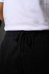 Close-up of white t-shirt tucked into black drawstring cargo pants with adjustable waist ties and side pockets.
