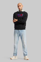 Full-body view of a man wearing a black Underrated graphic sweatshirt layered over a white collared shirt, light blue jeans, and white sneakers against a plain grey background.