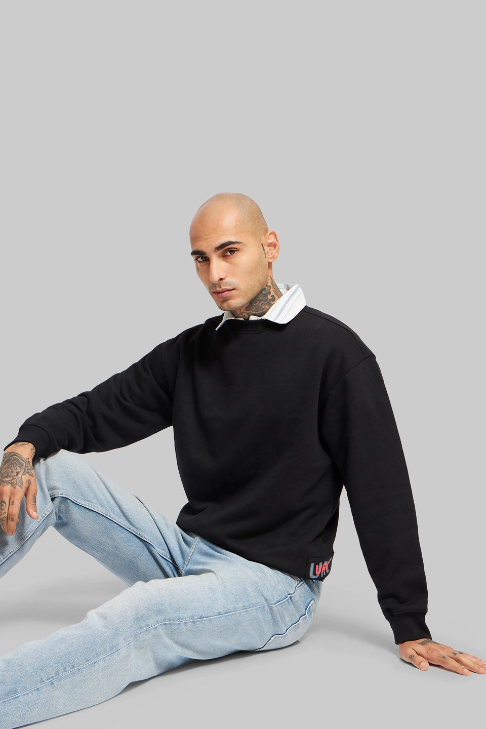 Front view of a man standing with arms crossed in a black oversized sweatshirt and light blue relaxed-fit jeans.