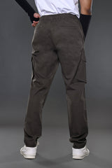 Back view of man in white t-shirt, charcoal grey drawstring UNDERRATED Club cargo pants with side flap pockets, wristbands, and white sneakers against grey background.