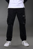 Full-body view of men's black UNDERRATED CLUB cargo pants with flap pockets and label patch, styled with white t-shirt and sneakers.