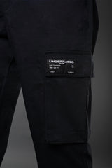 Close-up of black UNDERRATED cargo pants thigh pocket with woven label patch reading 