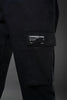 Close-up of black UNDERRATED cargo pants thigh pocket with woven label patch reading 