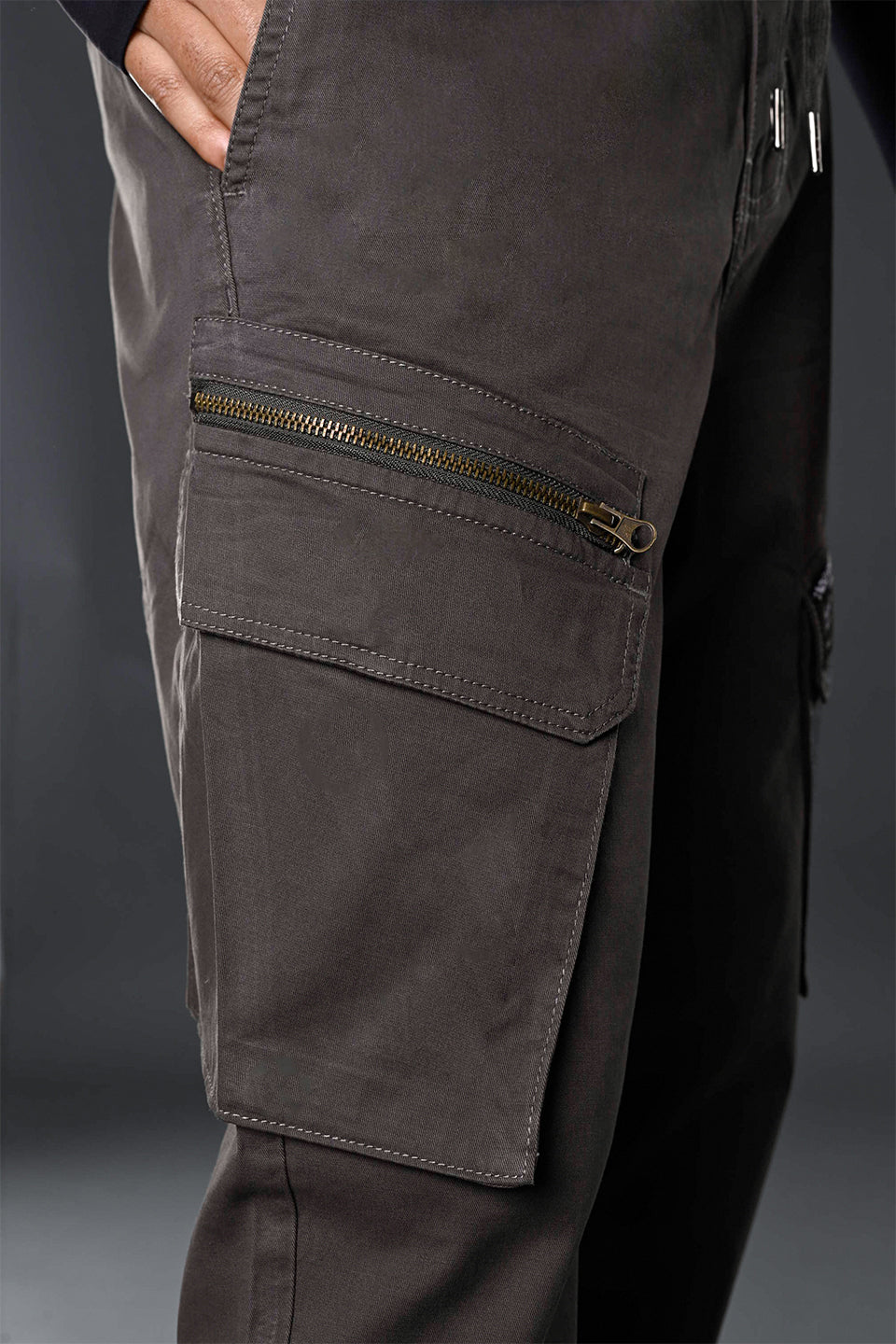 Close-up of charcoal grey UNDERRATED cargo pants side with zippered pocket and drawstring waist details.
