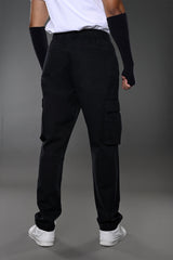 Back view of man in white t-shirt, black UNDERRATED CLUB cargo pants with side pockets, wristbands, and white sneakers.
