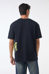 Back view of the black t-shirt showing a plain rear with just the edge of the yellow side graphic visible near the hem, paired with blue jeans.