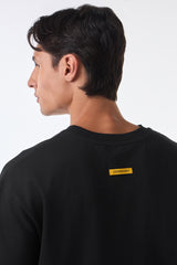 Man turning right shoulder view in black oversized t-shirt, arms relaxed, studio lighting.