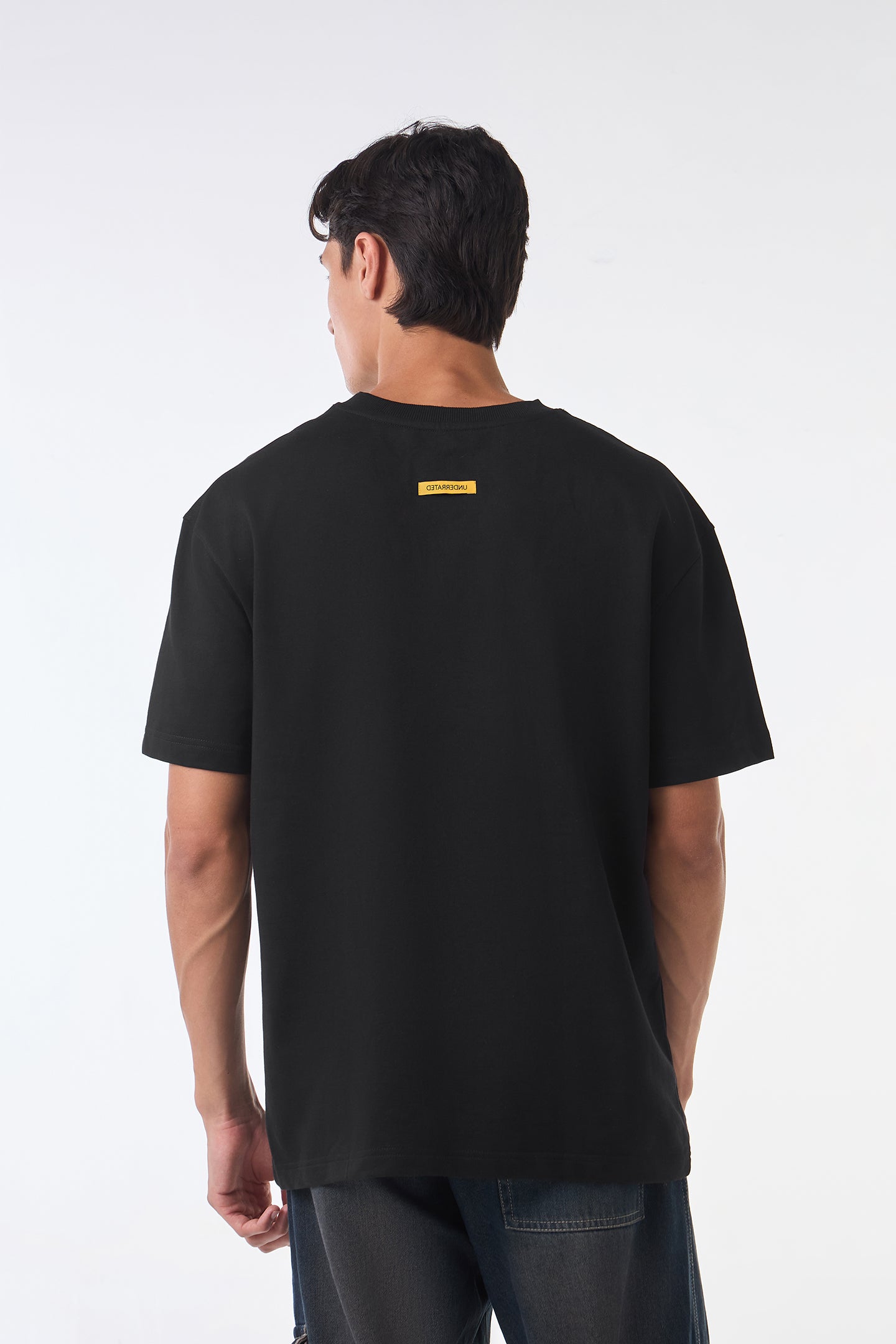 Man standing front view wearing black oversized crew neck t-shirt, hands at sides, neutral studio background.
