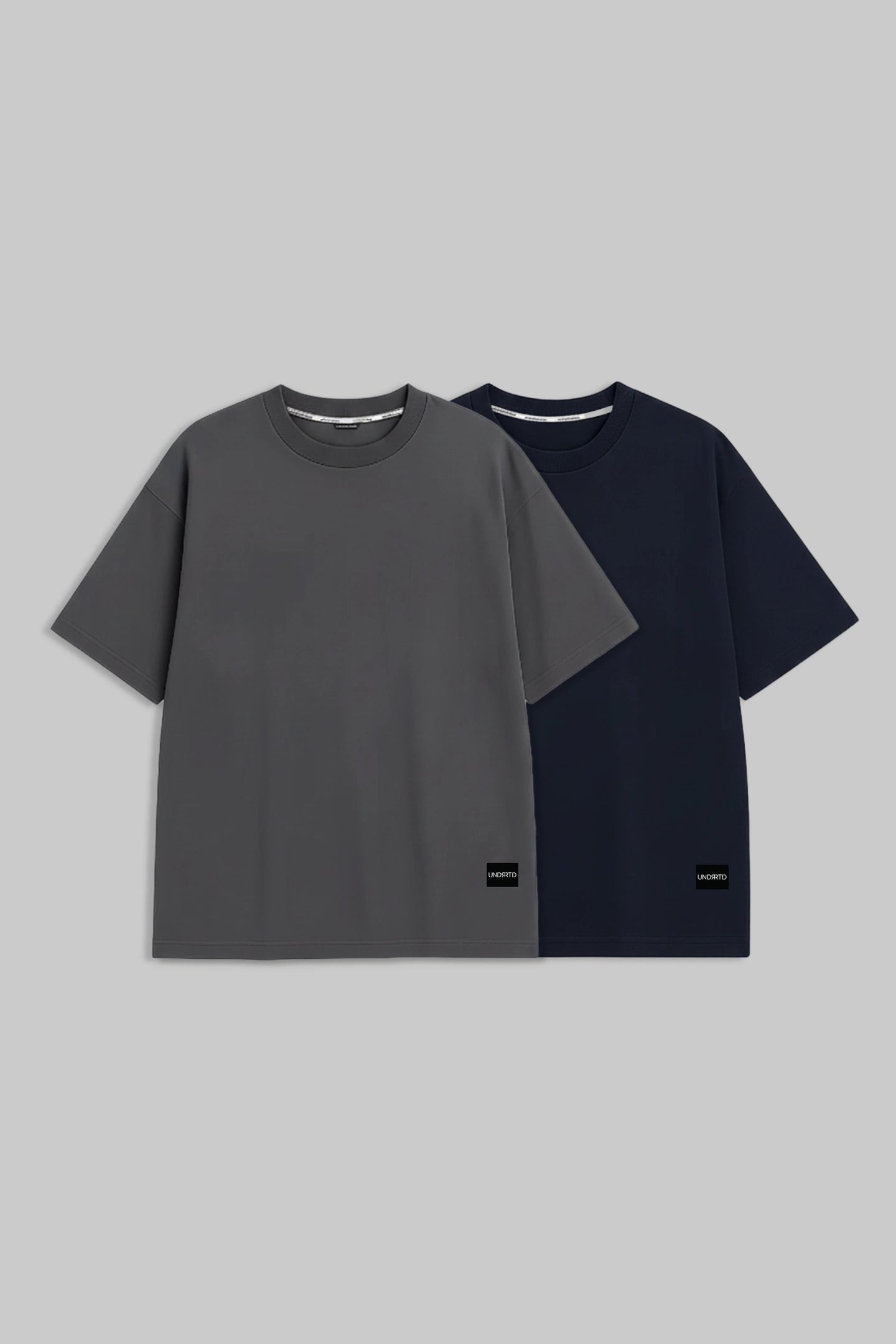 Two short-sleeve crewneck t-shirts displayed side by side on a solid gray background. The front t-shirt is dark gray, and the t-shirt behind it is navy blue.