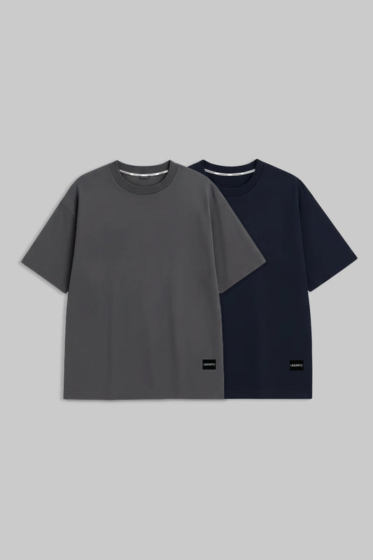 Two short-sleeve crewneck t-shirts displayed side by side on a solid gray background. The front t-shirt is dark gray, and the t-shirt behind it is navy blue.