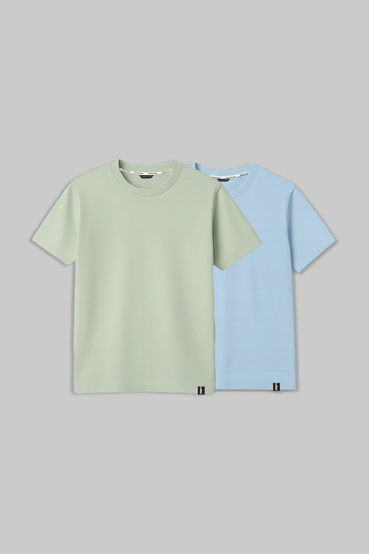 Two short-sleeve crew-neck t-shirts displayed flat against a solid gray background. The front shirt is a light sage green, and the shirt behind it is a light sky blue.