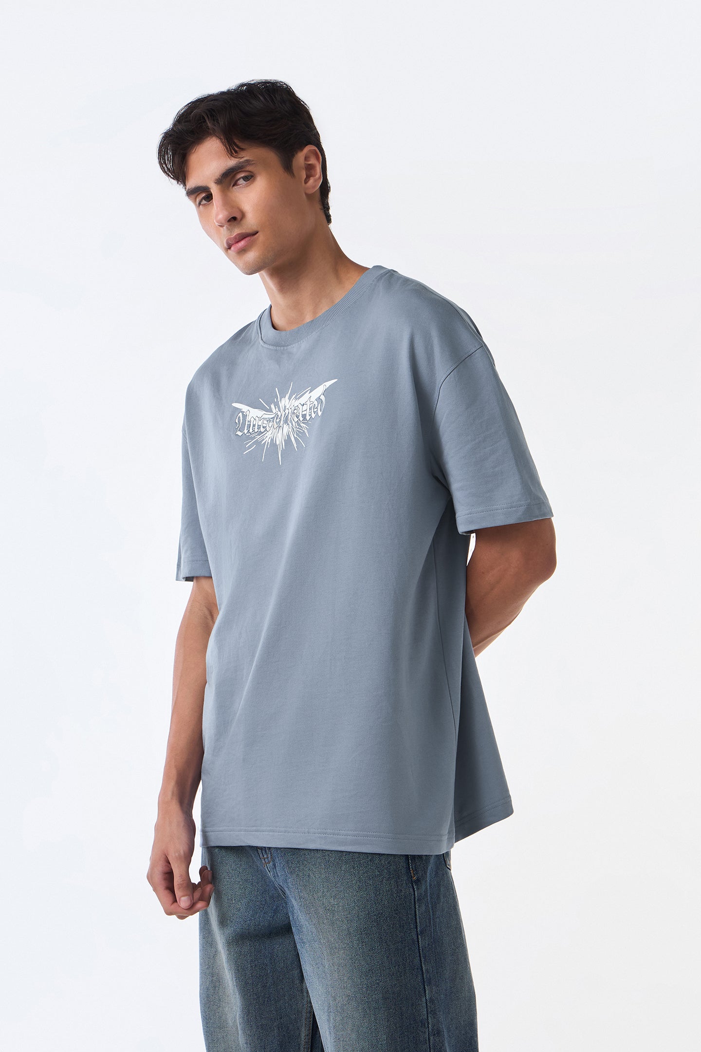 Man close-up front view wearing light grey oversized crew neck t-shirt, direct gaze, clean background.
