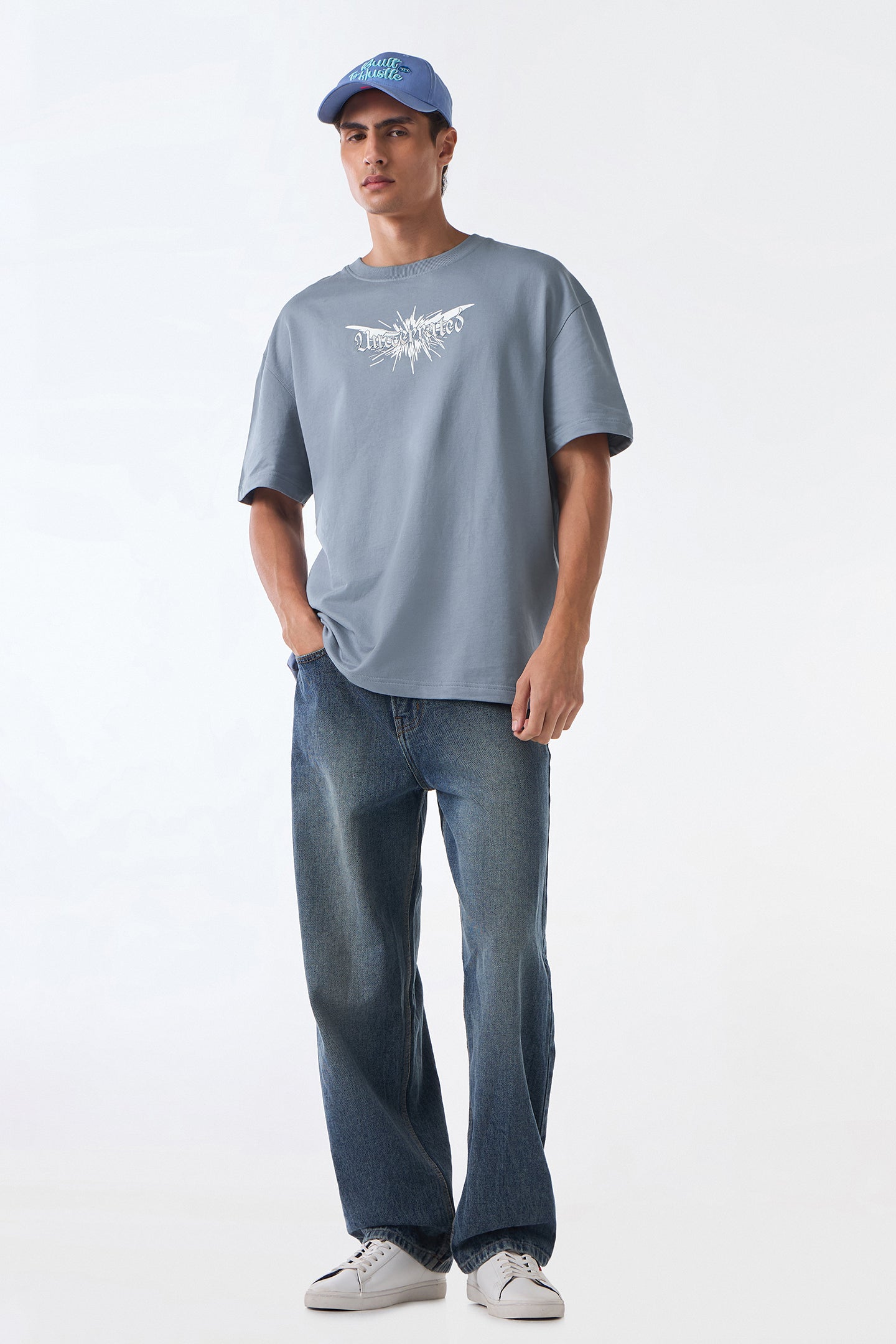 Man front view standing in light grey oversized t-shirt and jeans, hands at sides, neutral backdrop.
