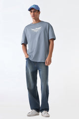 Man front view standing in light grey oversized t-shirt and jeans, hands at sides, neutral backdrop.
