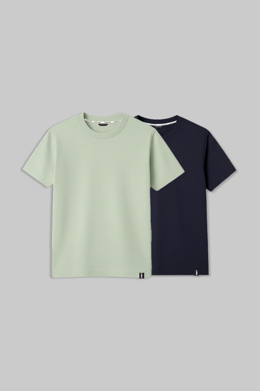 Two short-sleeve crew-neck t-shirts displayed flat against a solid gray background. The front t-shirt is a light sage green, and the t-shirt behind it is a dark navy blue.