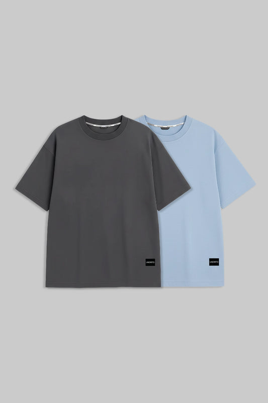 Two short-sleeve crewneck t-shirts displayed side-by-side against a solid gray background. The front t-shirt is dark charcoal gray, and the t-shirt behind it is light blue.