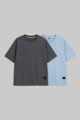Two short-sleeve crewneck t-shirts displayed side-by-side against a solid gray background. The front t-shirt is dark charcoal gray, and the t-shirt behind it is light blue.