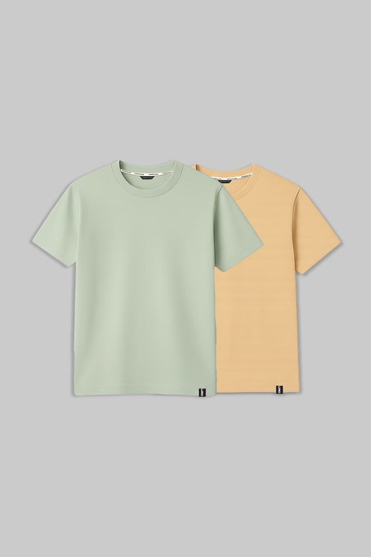 Two short-sleeve crew-neck t-shirts displayed flat against a solid gray background. The front t-shirt is a light sage green, and the t-shirt behind it is a soft peachy yellow.