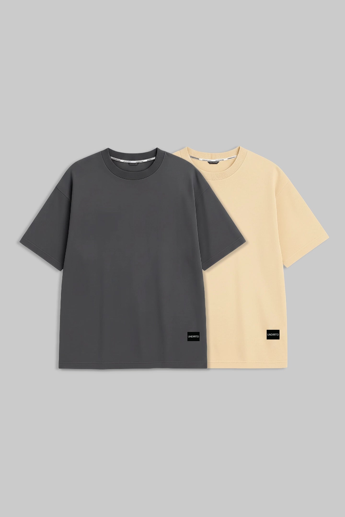 Two plain short-sleeve crew-neck T-shirts on a light gray background, shown overlapping. The front shirt is dark charcoal gray, and the shirt behind it is pale cream/yellow.