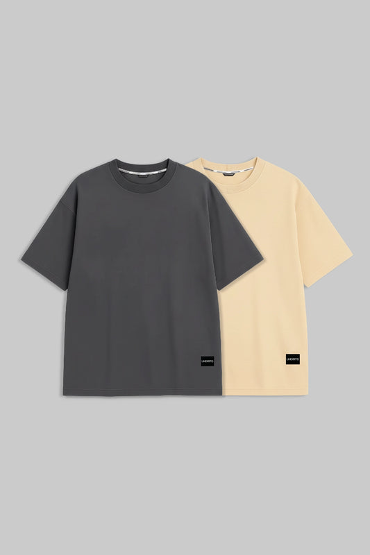 Two plain short-sleeve crew-neck T-shirts on a light gray background, shown overlapping. The front shirt is dark charcoal gray, and the shirt behind it is pale cream/yellow.