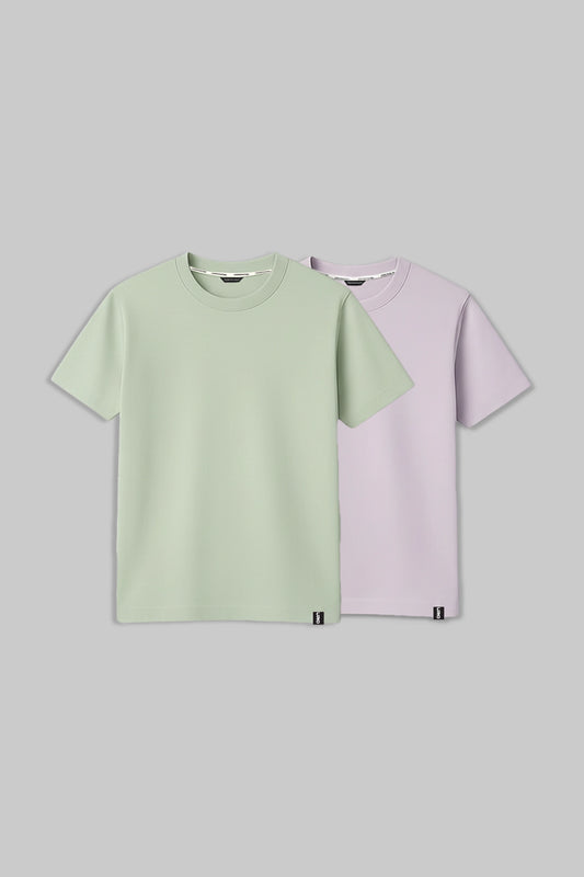 Two short-sleeve crew-neck t-shirts displayed flat against a solid gray background. The front t-shirt is a light sage green, and the t-shirt behind it is a pale lavender purple.