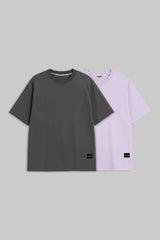 Two short-sleeve crewneck t-shirts displayed side-by-side on a solid gray background. The front t-shirt is dark charcoal gray, and the t-shirt behind it is light lavender purple.