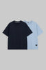 Two short-sleeve crew-neck t-shirts displayed flat against a solid gray background. The front t-shirt is solid navy blue, and the t-shirt behind it is solid light blue.