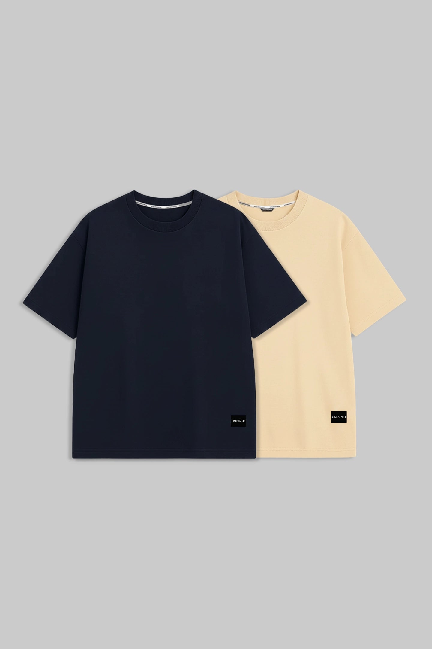 Two short-sleeve crew-neck t-shirts displayed flat against a solid gray background. The front t-shirt is dark navy blue, and the t-shirt behind it is a light cream/beige color.