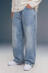 A person wearing light-wash, wide-leg denim jeans with a faded wash, styled with a cream long-sleeve top and white sneakers against a studio backdrop.