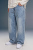 A person wearing light-wash, wide-leg denim jeans with a faded wash, styled with a cream long-sleeve top and white sneakers against a studio backdrop.