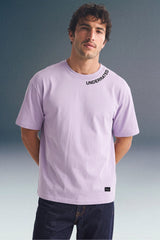 Front view from the waist up of a man standing straight, wearing a light purple T-shirt featuring small black text along the collar seam.