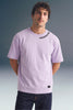 Front view from the waist up of a man standing straight, wearing a light purple T-shirt featuring small black text along the collar seam.
