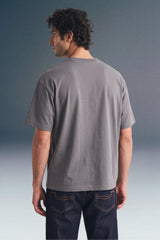 Rear view from the waist up of a man looking over his left shoulder, showcasing the fit of a plain dark grey T-shirt paired with dark blue jeans.