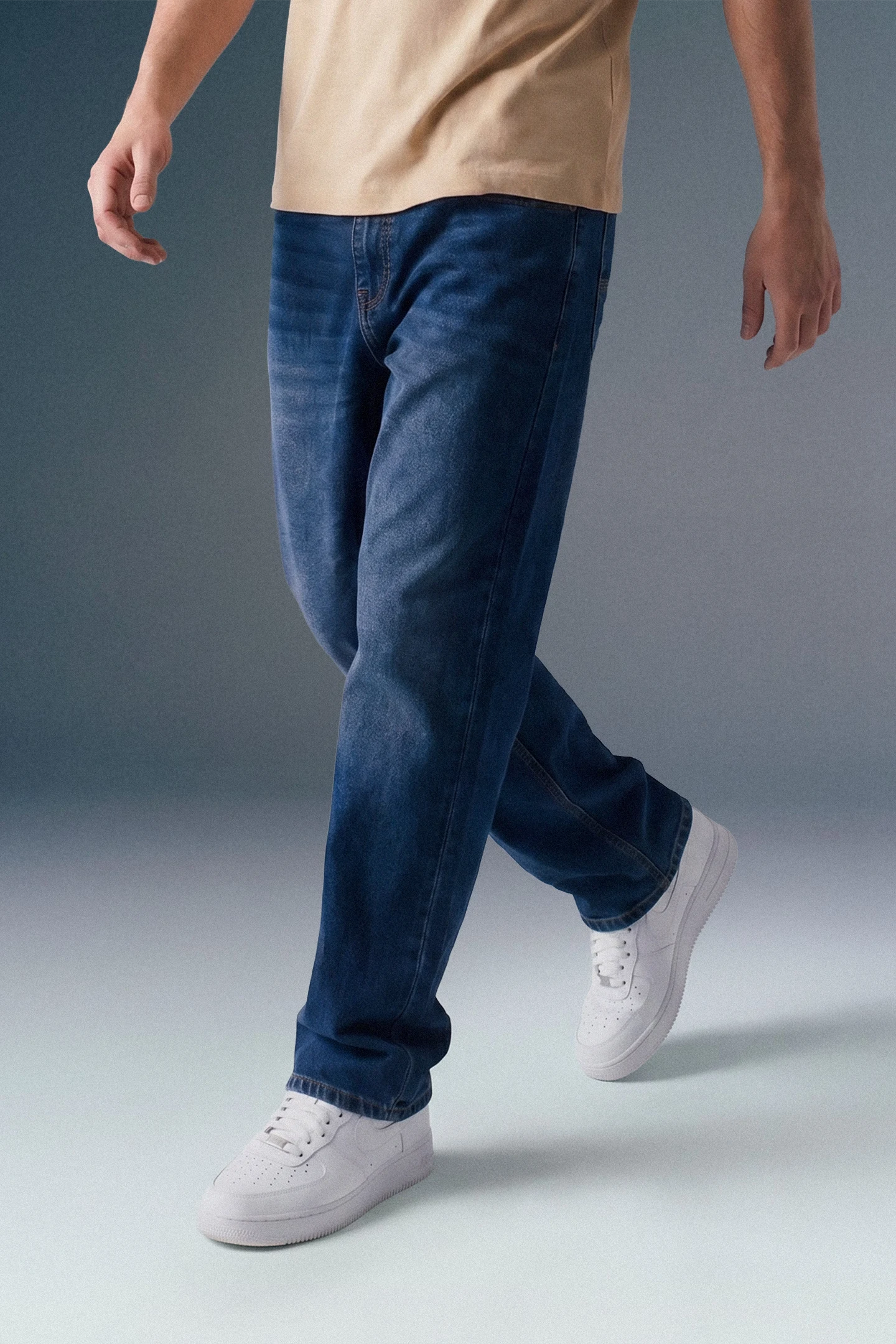 Person wearing blue jeans and white sneakers on a gradient background