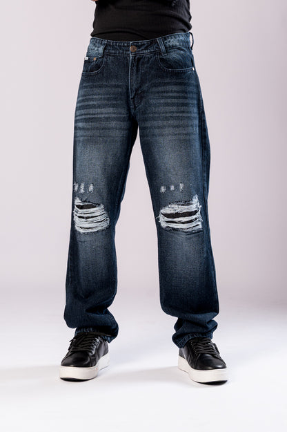 Front view of a person's lower body, showing dark-wash blue baggy jeans with ripped knees and black sneakers.